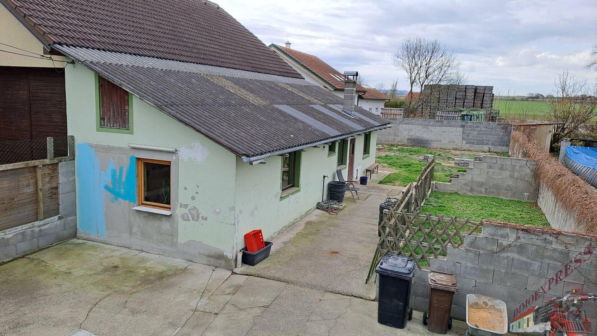 Ein Hinterhof mit Rasenfläche, Betonweg und einem älteren Gebäude im Hintergrund.