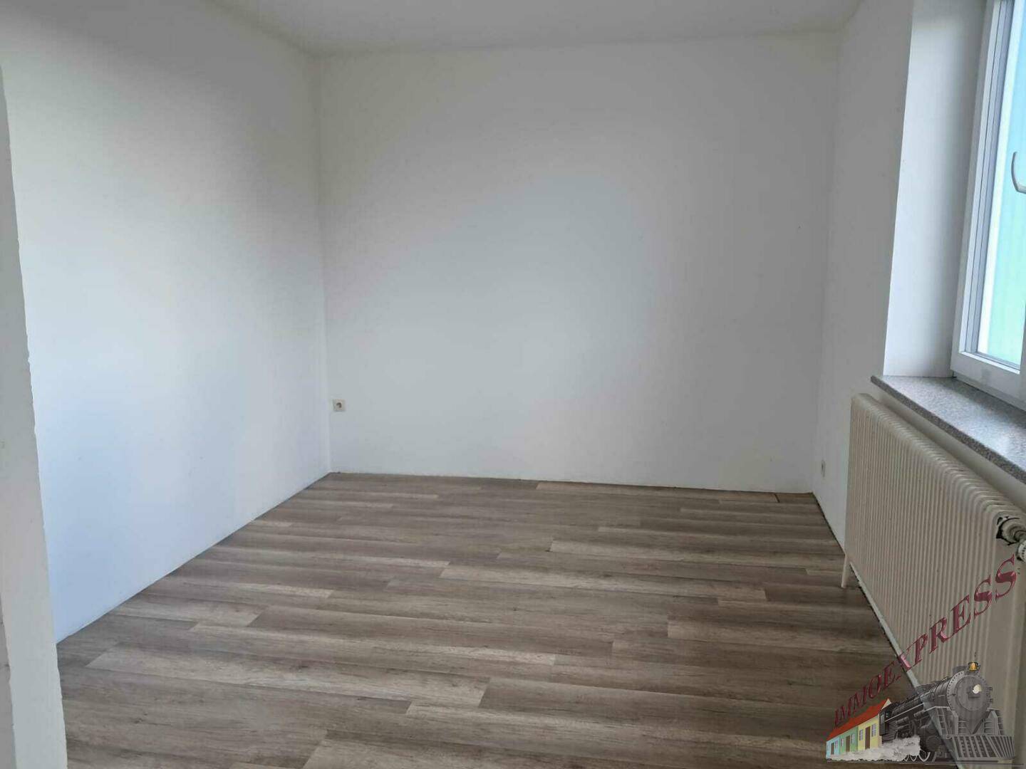 Ein leerer Raum mit Laminatboden und weißen Wänden, bereit für eine Renovierung.