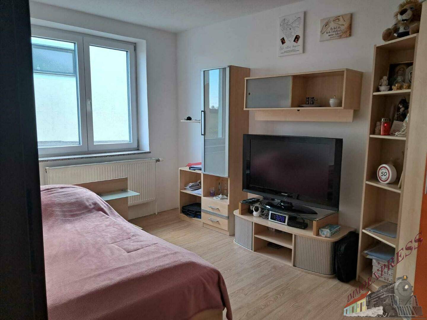 Ein Schlafzimmer mit Bett, Schrank und großem Fenster, das viel Tageslicht hereinlässt.