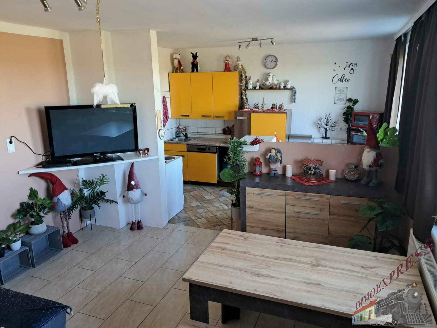 Ein offener Wohnbereich mit Esstisch und Fernseher grenzt an die gelbe Küche.