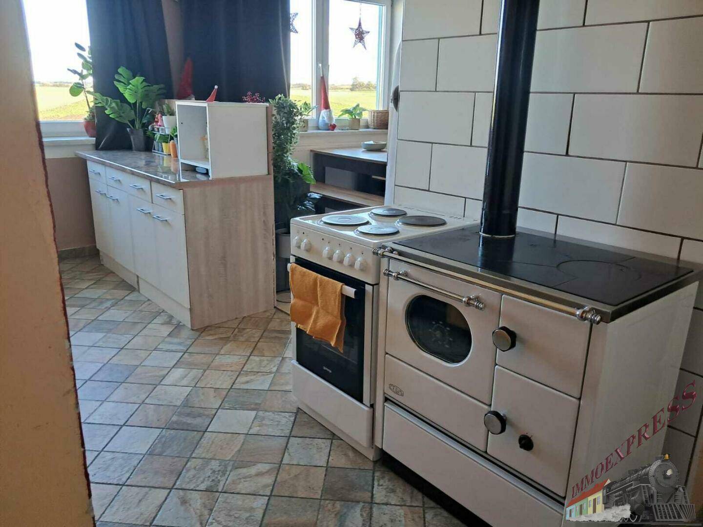 Die Küche zeigt einen traditionellen Kachelofen neben einem modernen Elektroherd und Blick ins Grüne.