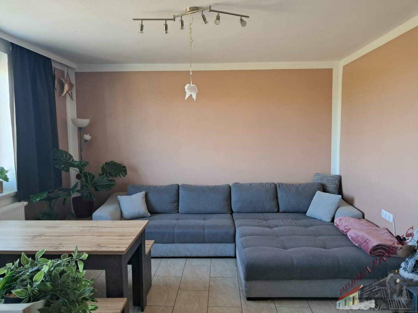 Das Wohnzimmer ist mit einem großen grauen Ecksofa und einem Esstisch ausgestattet.