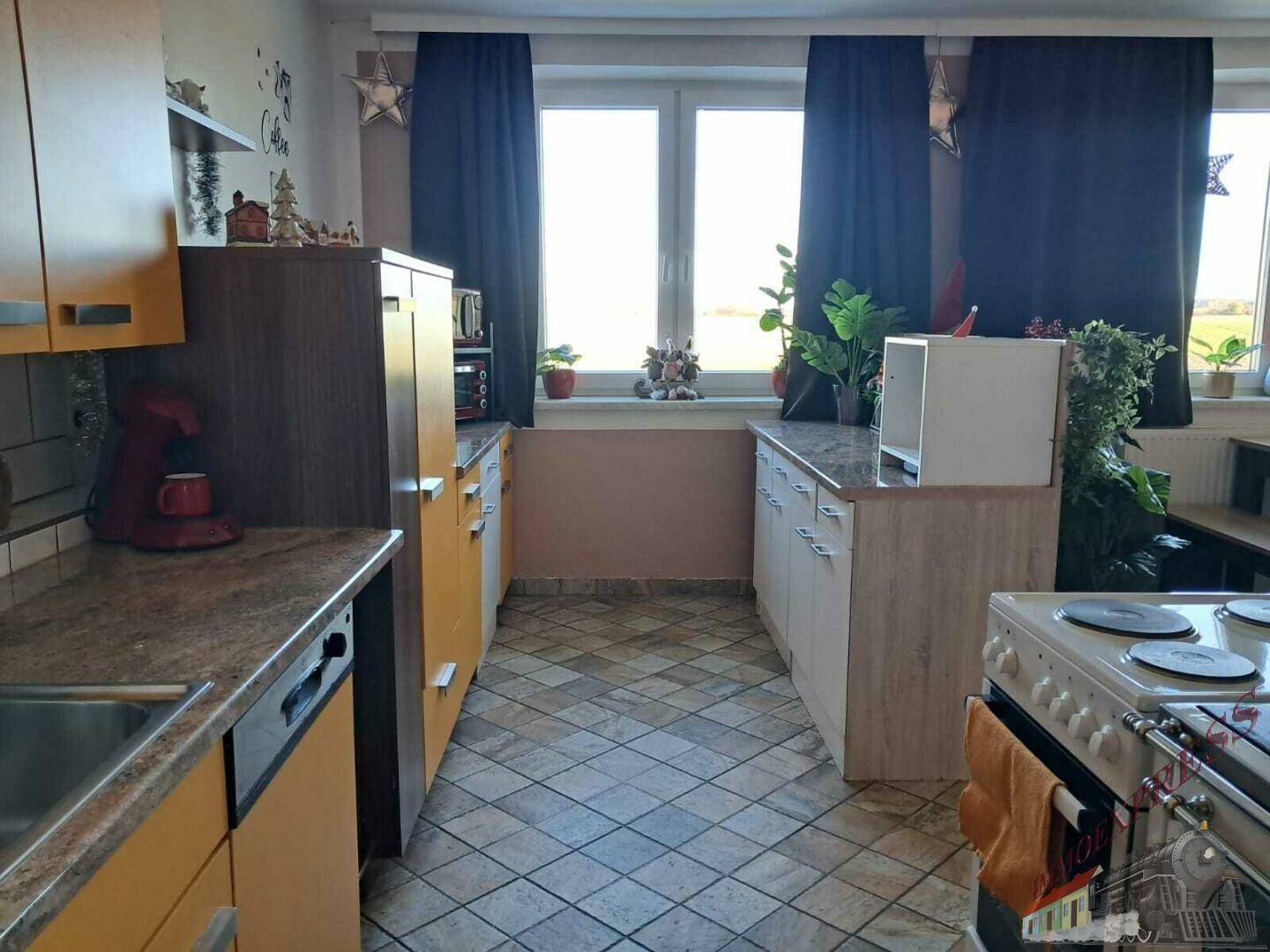 Die Küche verfügt über gelbe Einbauschränke, Fliesenboden und einen weiten Blick ins Grüne.