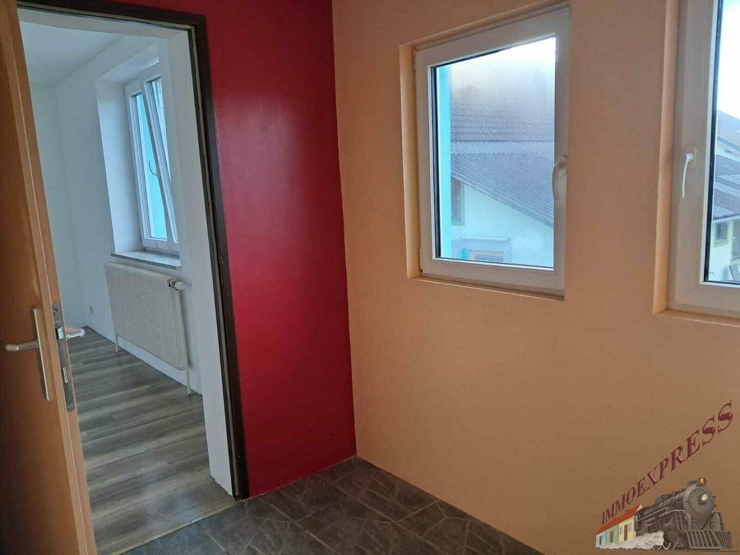 Ein kleiner Flur mit roter Akzentwand führt in einen weiteren Raum mit Laminatboden.