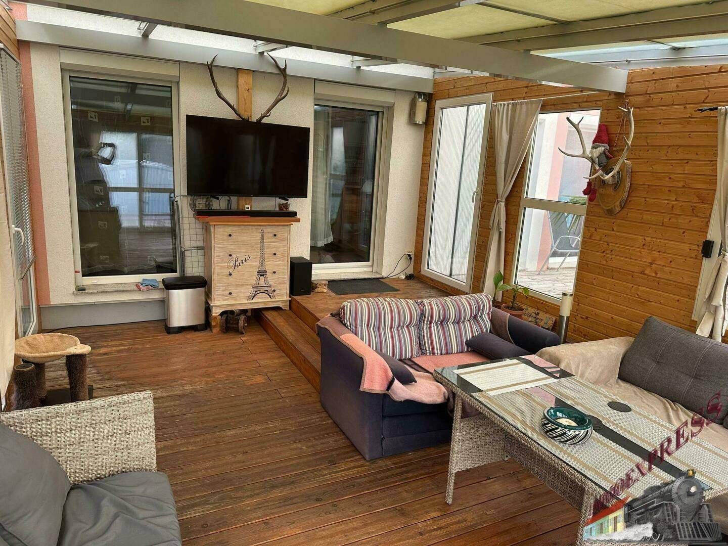 Gemütlicher Wintergarten mit Holzverkleidung, Fernseher und Blick in den Garten.