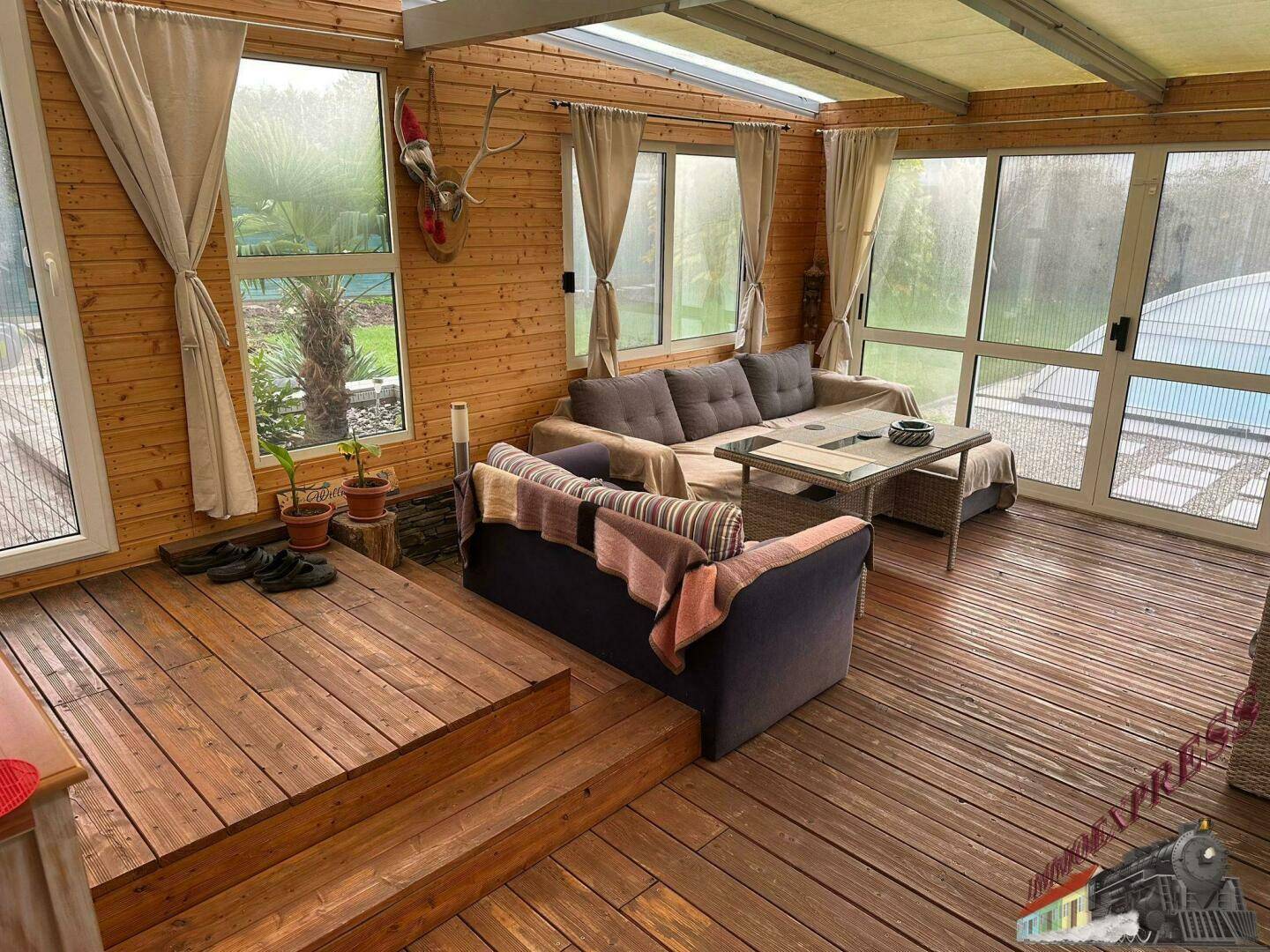 Heller Wintergarten mit Holzverkleidung, bequemen Sofas und Blick in den Garten.