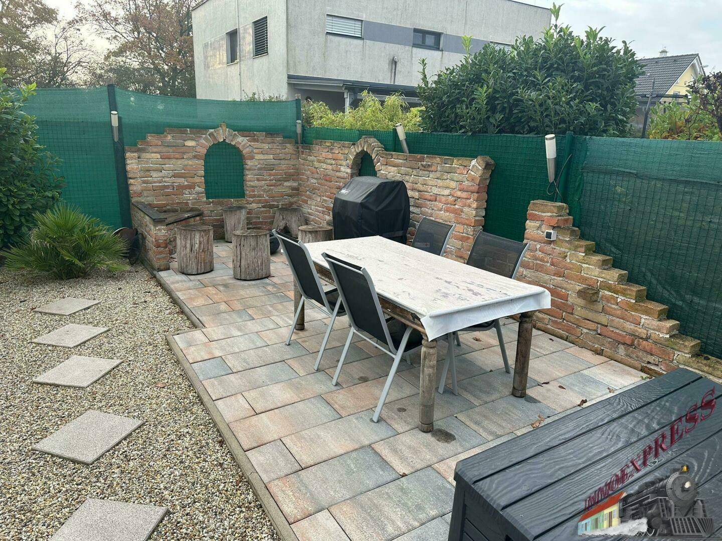 Gemütlicher Essbereich im Freien mit großem Tisch und Stühlen, umgeben von einer Ziegelmauer.