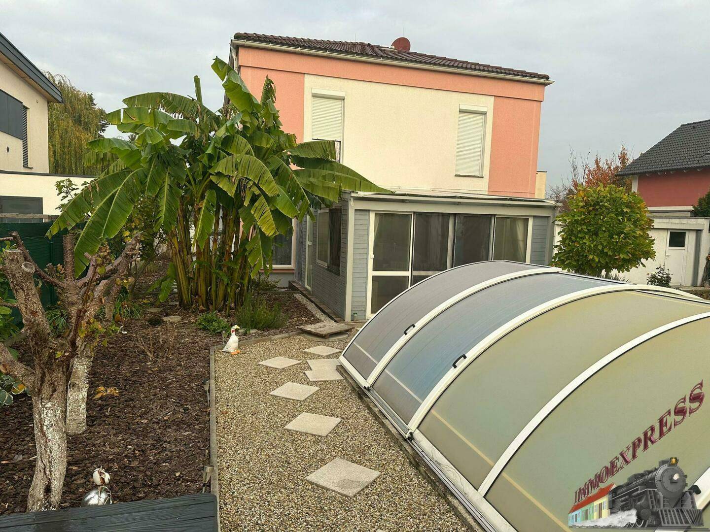 Gartenansicht mit üppiger Bepflanzung, Rasenfläche und der Abdeckung des Swimmingpools.