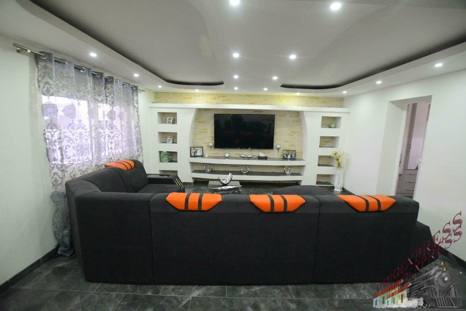 Modernes Wohnzimmer mit großer Couch, Wandfernseher und indirekter Beleuchtung.