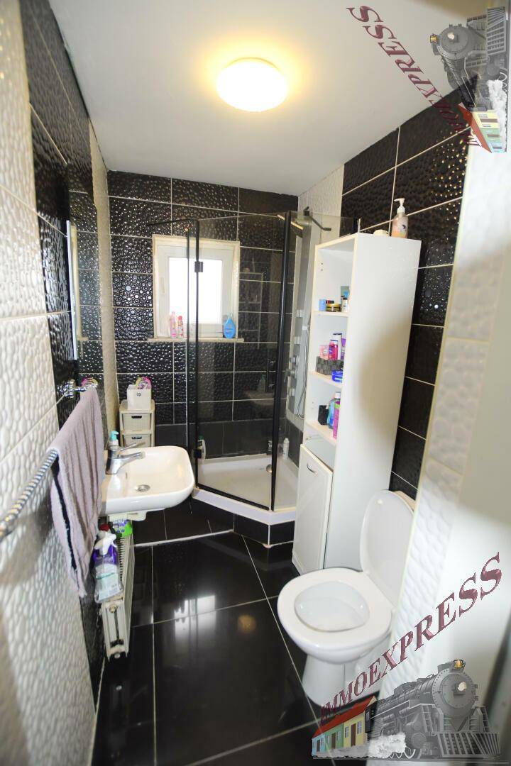 Modernes Badezimmer mit Duschkabine, schwarz-weißen Fliesen und kleinem Waschbecken.