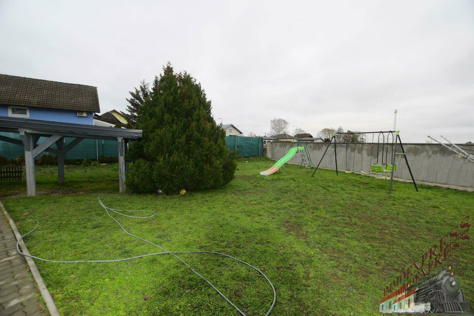 Großer Garten mit Rasenfläche, Spielplatz und hohen Bäumen.