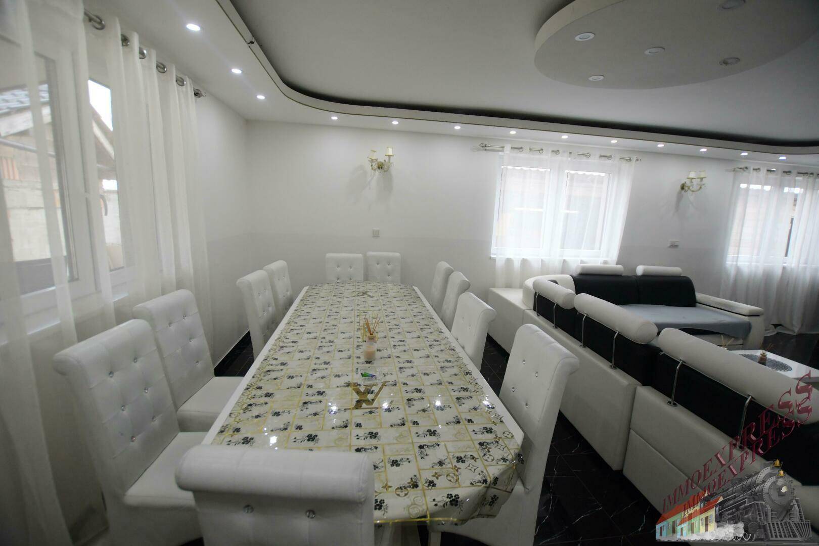 Eleganter Essbereich mit großem Esstisch, weißen Stühlen und dunklem Fliesenboden.