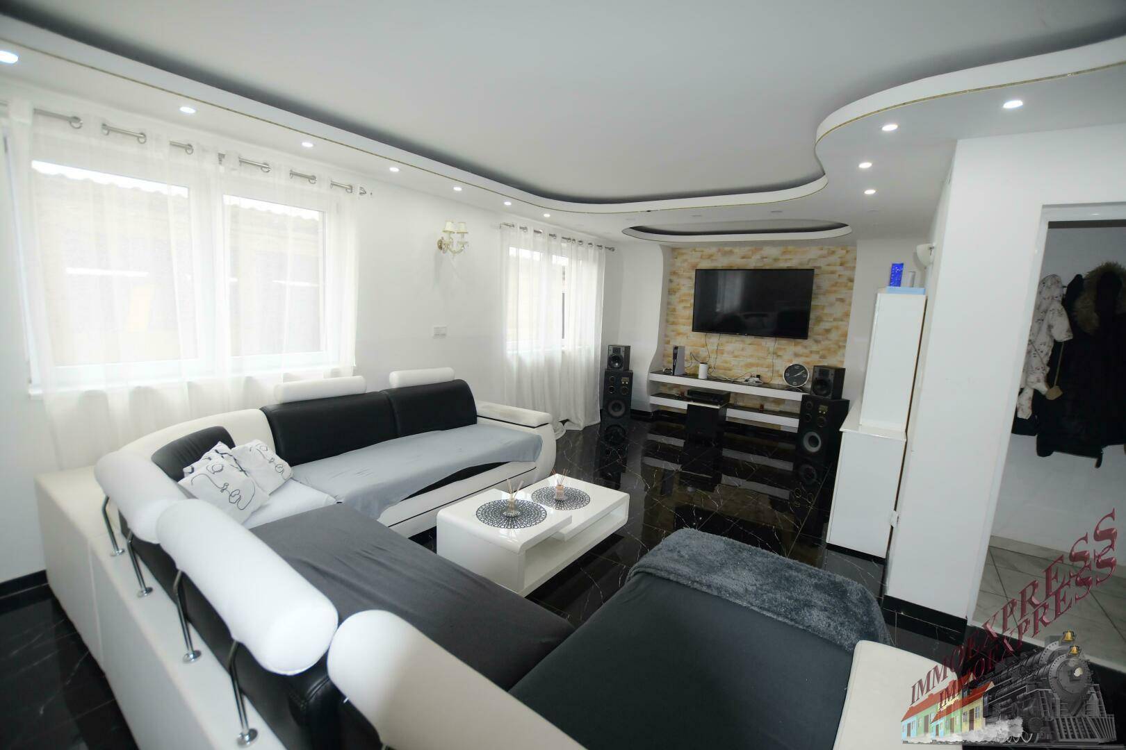Geräumiges Wohnzimmer mit großer Eckcouch, Fernseher und dunklem Fliesenboden.