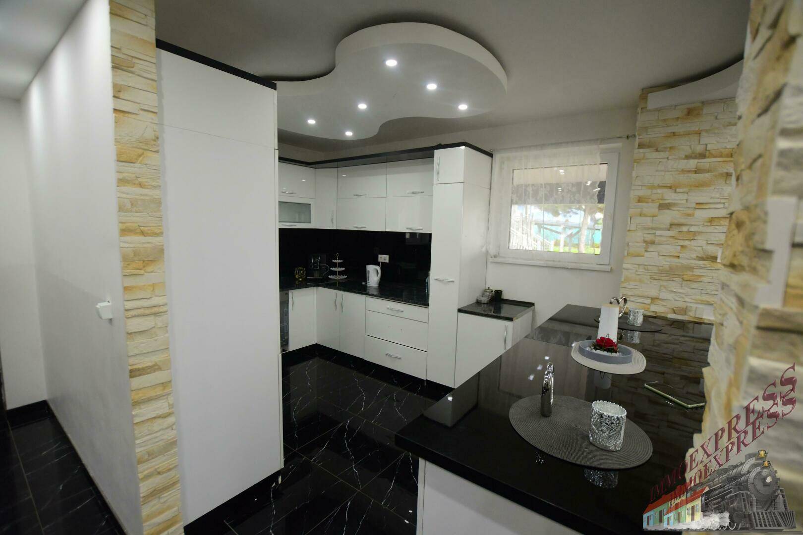 Moderne Küche mit weißen Schränken, schwarzen Arbeitsplatten und dekorativen Steinwand-Akzenten.