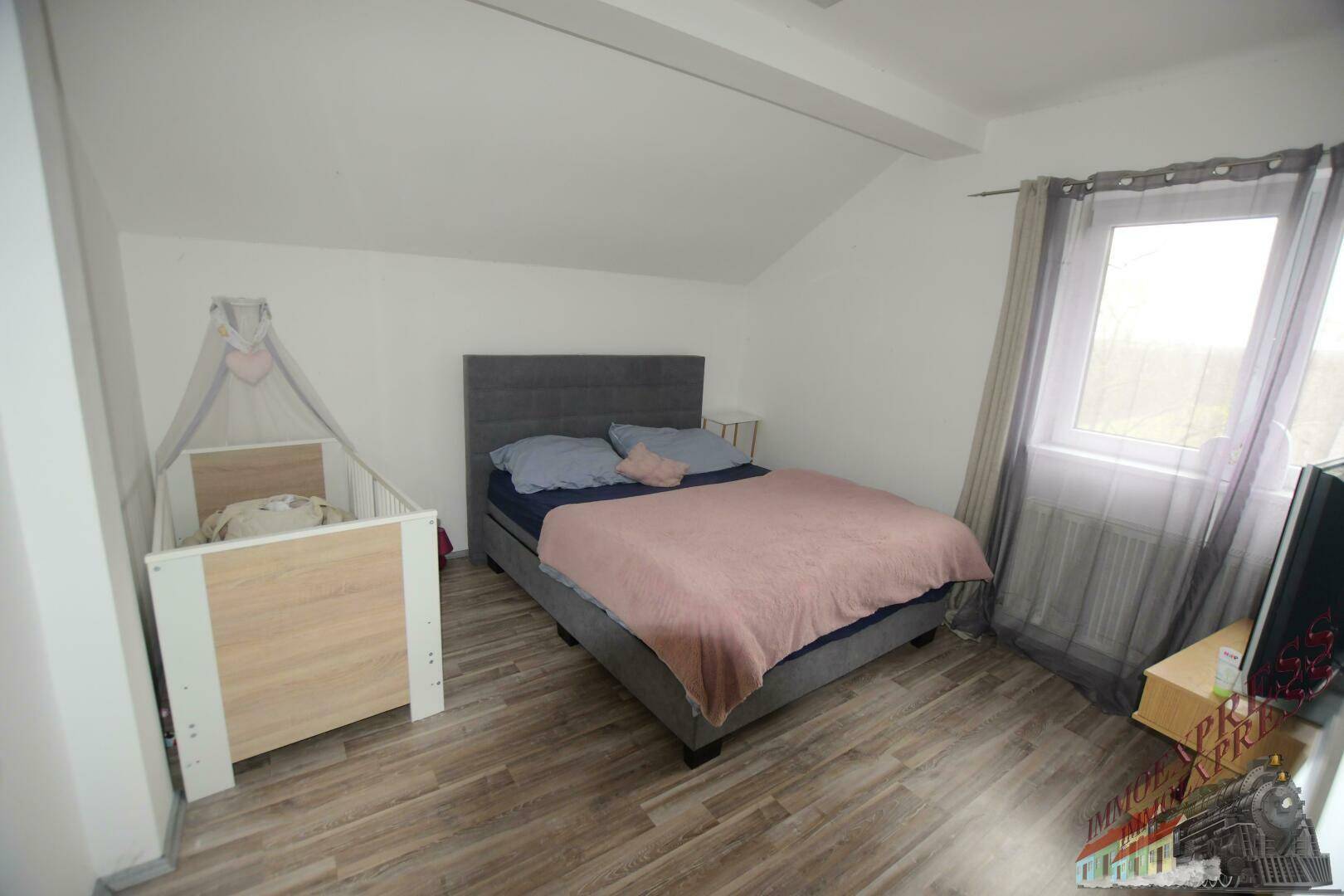 Geräumiges Schlafzimmer im Dachgeschoss mit Doppelbett, Babybett und Laminatboden.