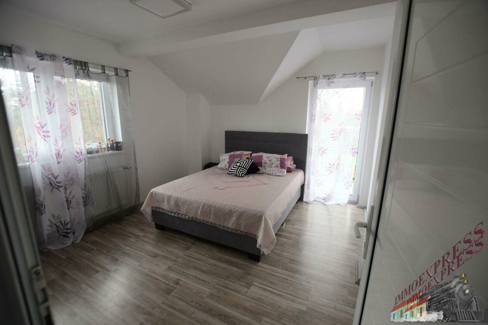 Helles Schlafzimmer mit Doppelbett, Laminatboden und Zugang zu einem französischen Balkon.