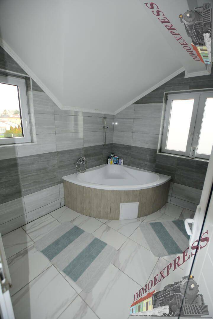 Helles Badezimmer im Dachgeschoss mit Eckbadewanne, modernen Fliesen und Fenster.