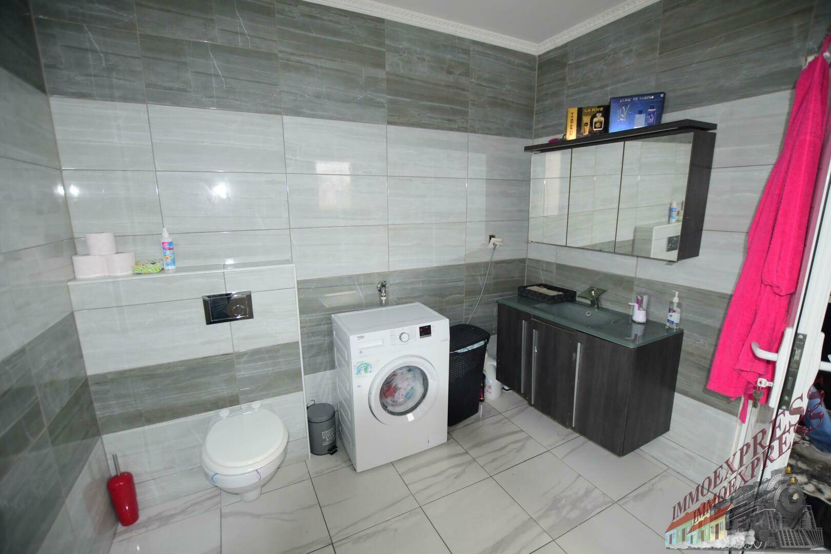 Modern gefliestes Badezimmer mit Toilette, Waschbecken, Spiegelschrank und Waschmaschine.
