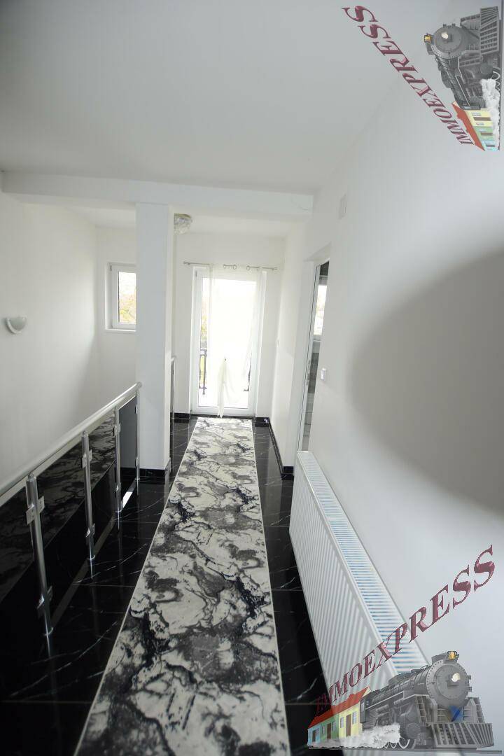 Heller Flur mit dunklem Fliesenboden, modernem Treppengeländer und Zugang zu einem französischen Balkon.