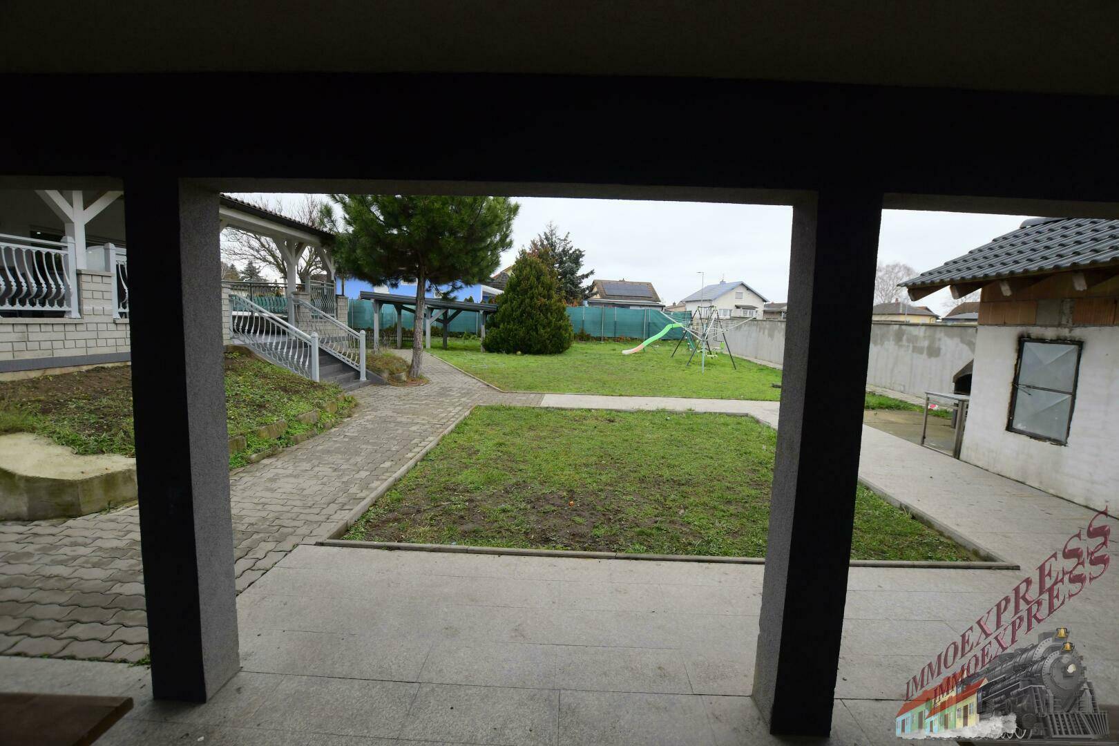 Blick vom überdachten Bereich in den Garten mit Rasenfläche und Kinderspielplatz.