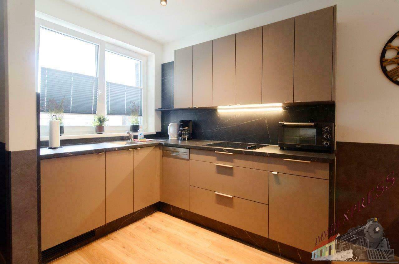 Moderne Einbauküche mit dunkler Arbeitsplatte, Induktionskochfeld und Fenster.