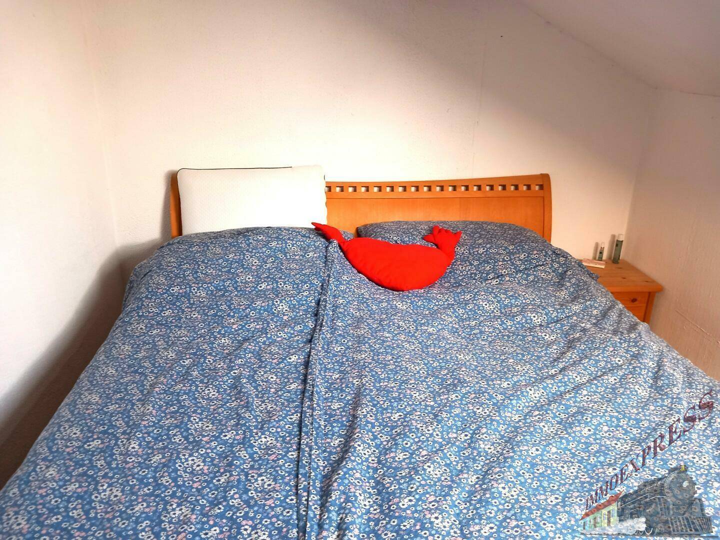 Schlafzimmer mit Holzbett und schlichter Einrichtung unter Dachschräge.