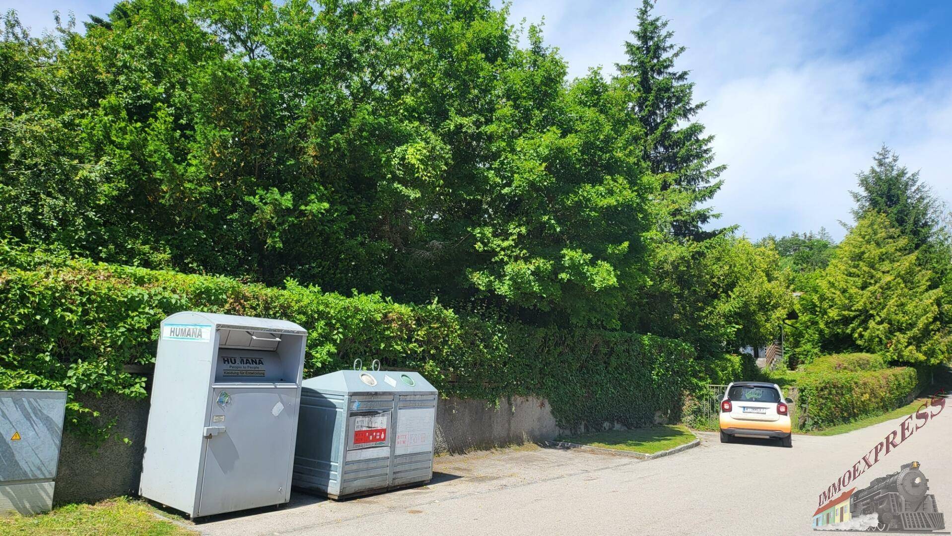 Blick auf die ruhige Anliegerstraße mit Recyclingcontainern und einem geparkten Auto.