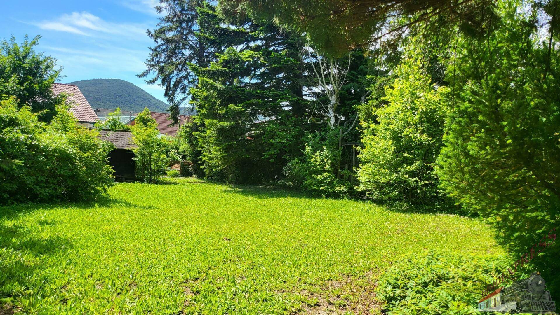 Weitläufige Rasenfläche im Garten mit Blick auf die grüne Umgebung und ferne Hügel.