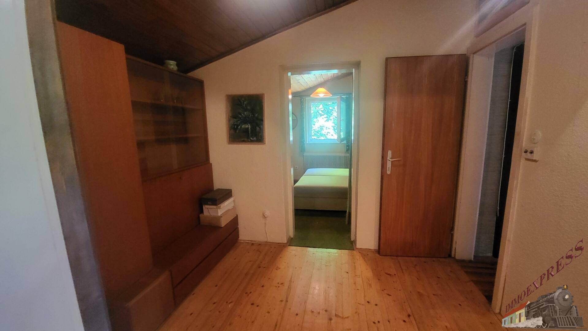 Flur mit Holzfußboden und Zugang zu einem weiteren Zimmer, unter einer Holzdecke.