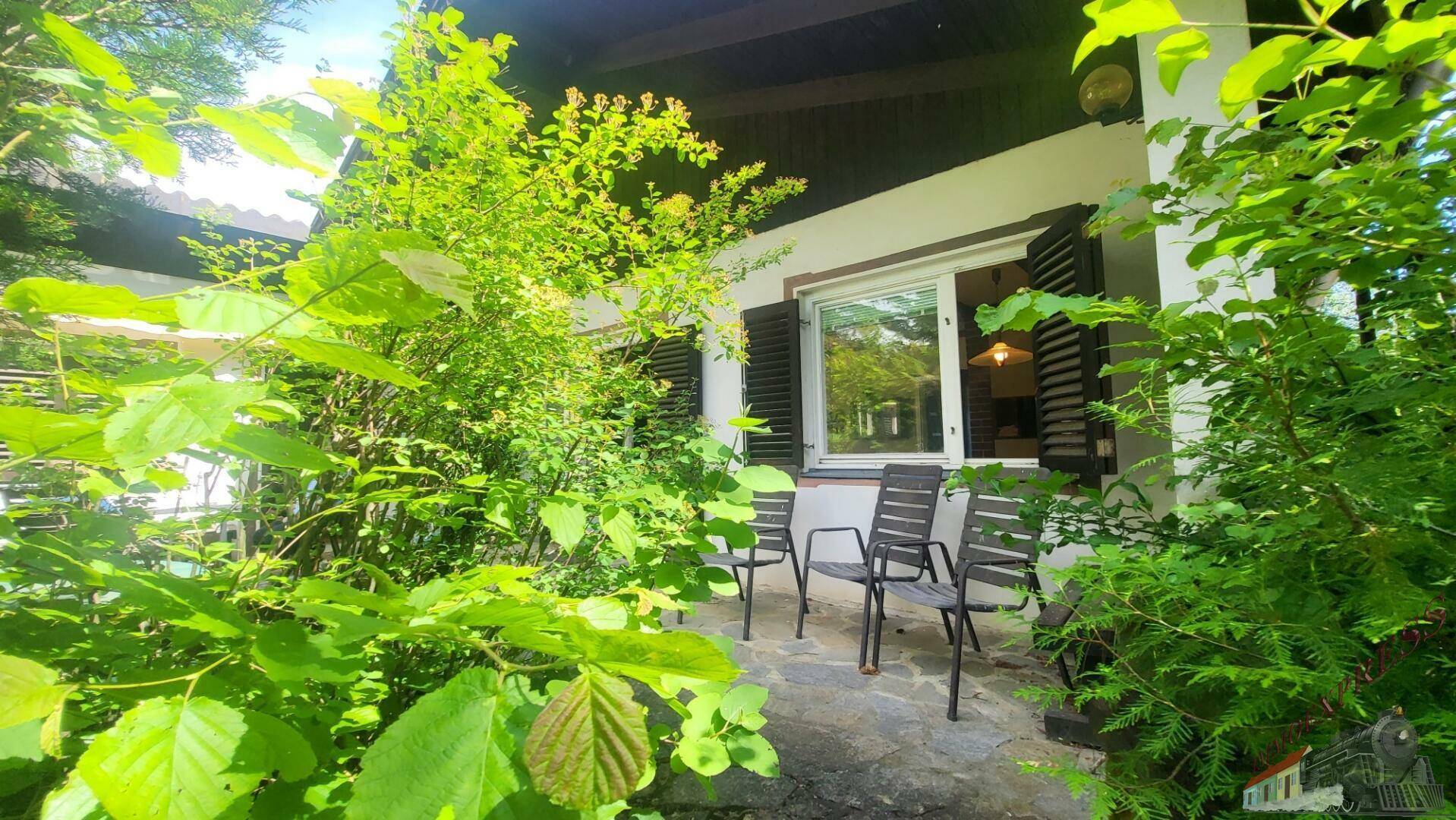 Sonnige Terrasse umgeben von üppigem Grün, ideal für entspannte Stunden im Freien.
