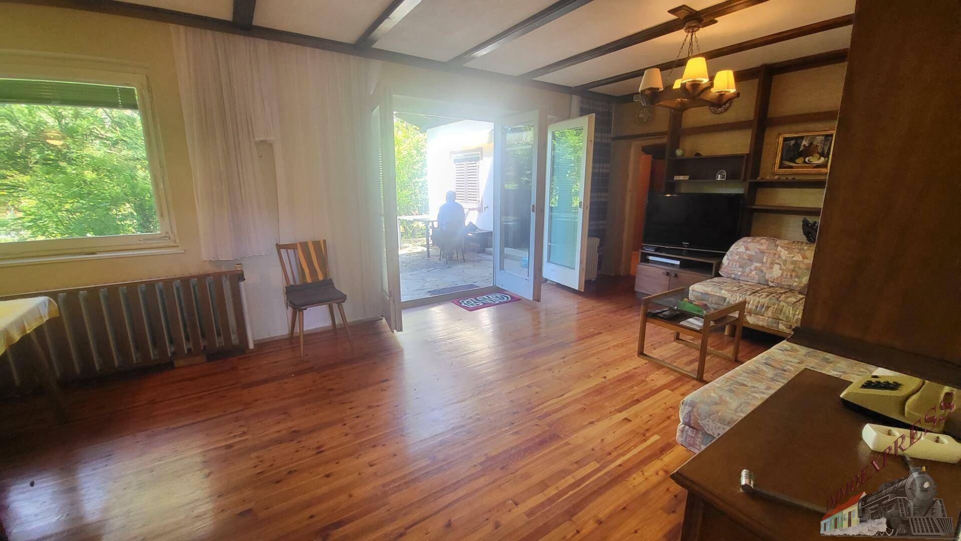 Helles Wohnzimmer mit Holzboden, großem Fenster und Zugang zum Außenbereich.