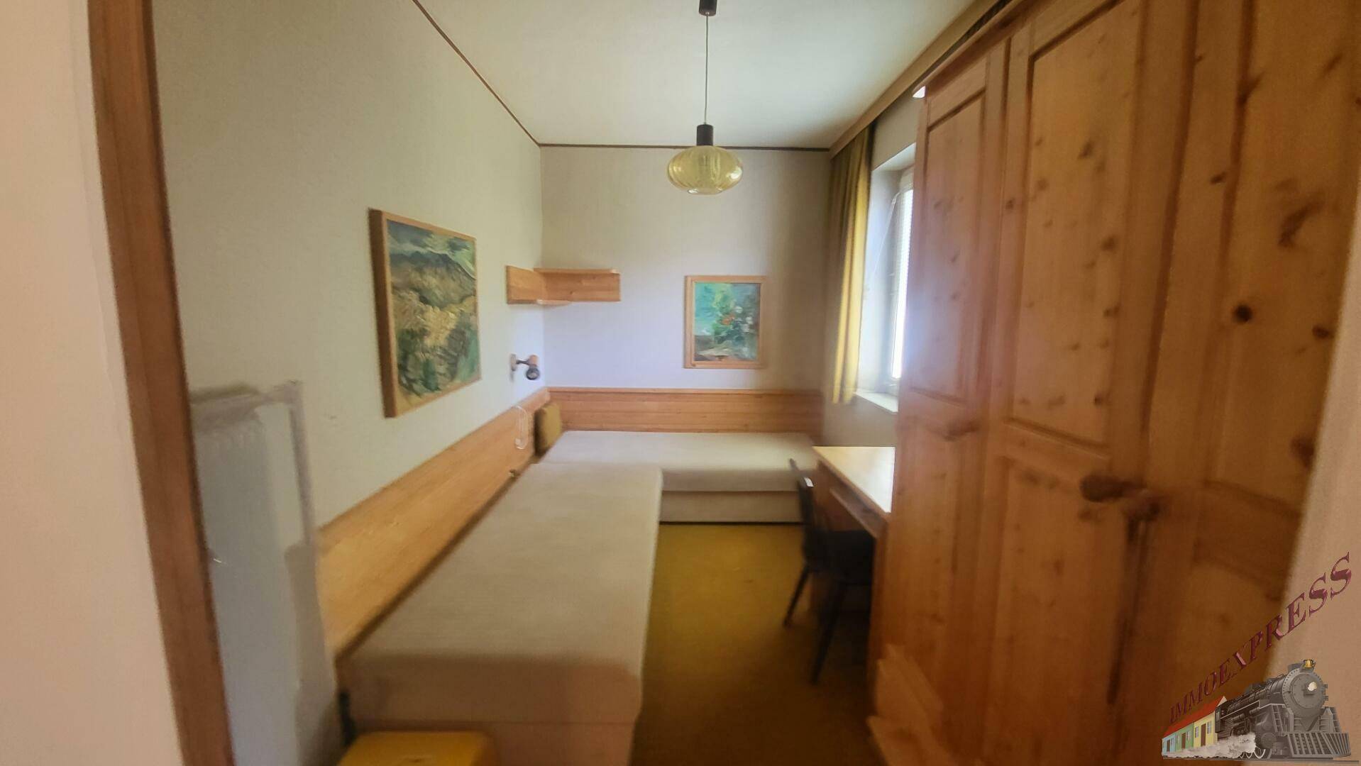 Schlafzimmer mit Einzelbetten, Holzschrank und Fenster, das Tageslicht hereinlässt.