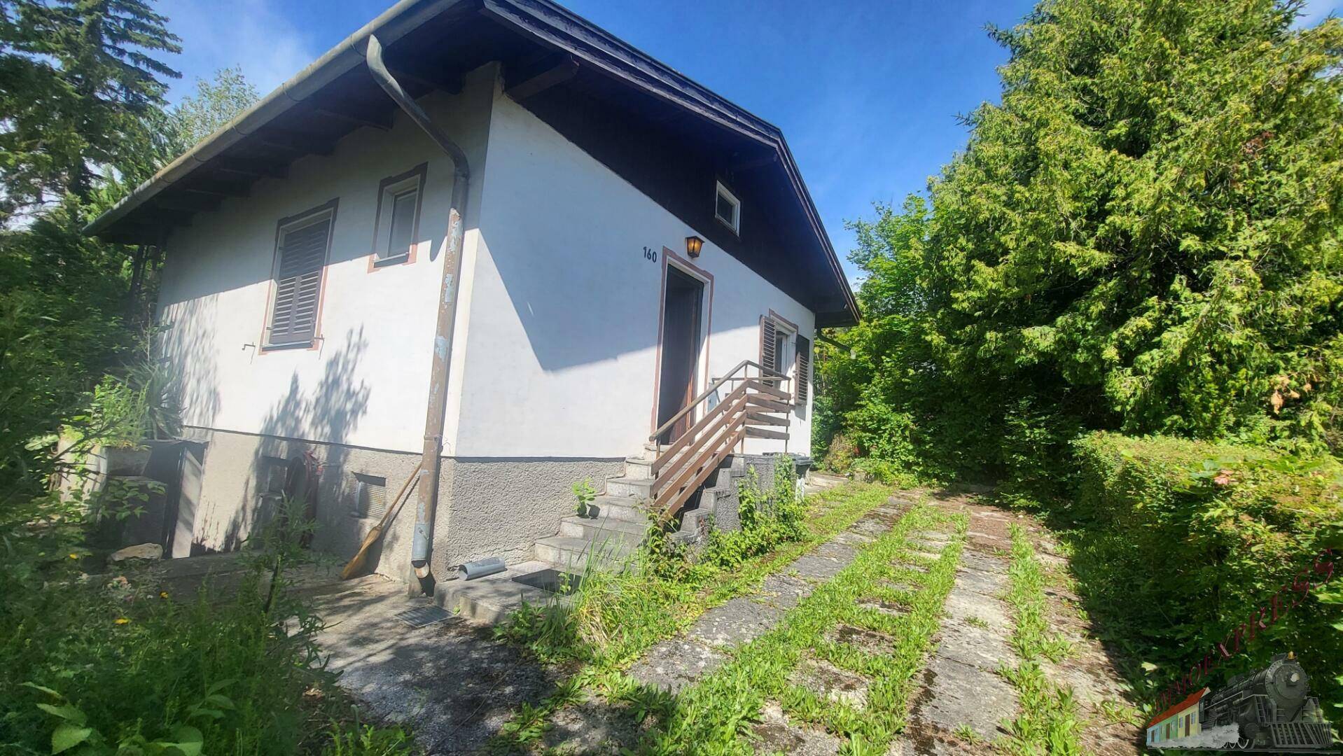 Seitenansicht des Hauses mit Zufahrt und Außentreppe, umgeben von Natur.