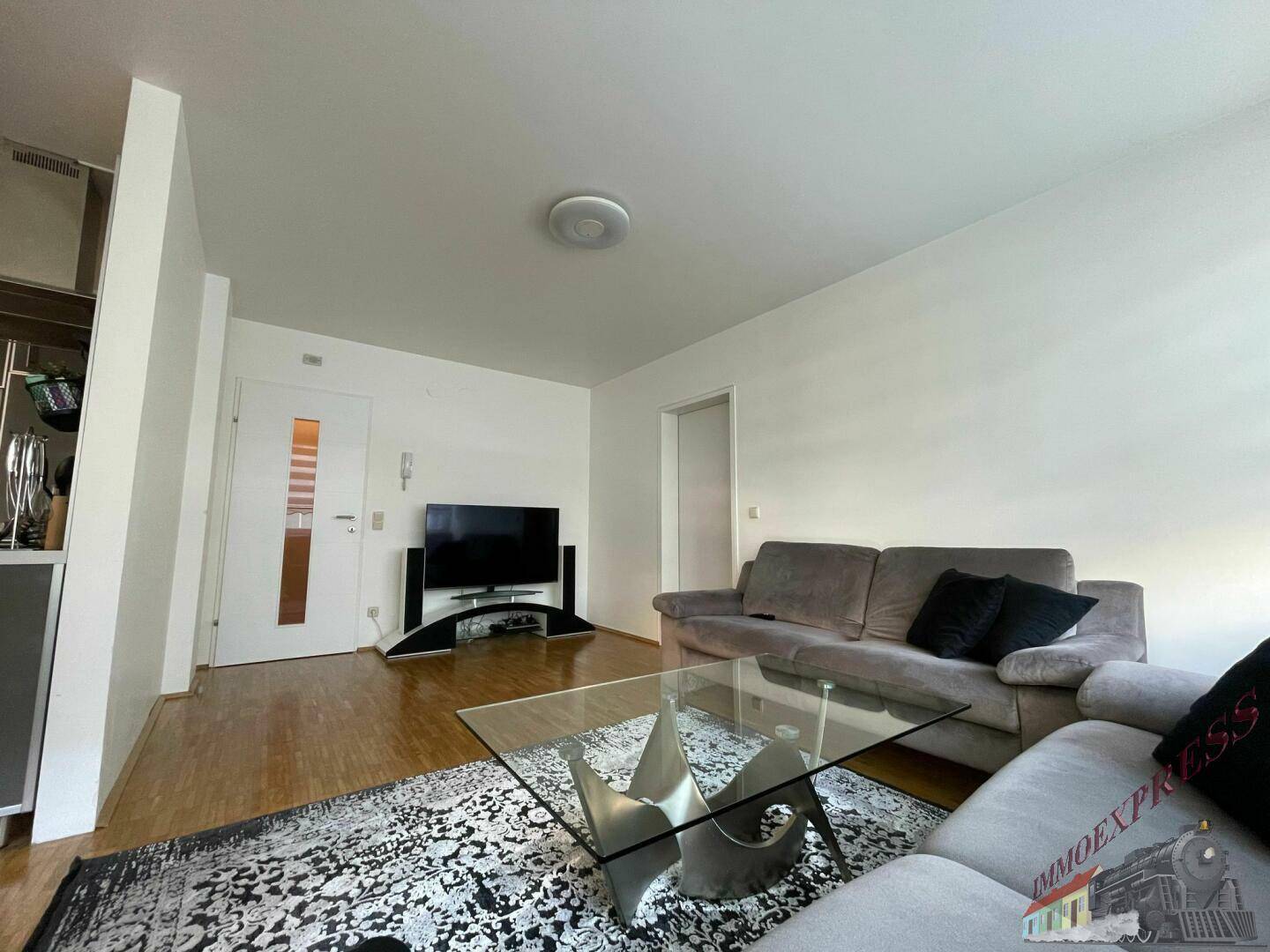Wohnzimmer mit großem Sofa, Glastisch und Fernseher, offen zum Essbereich.