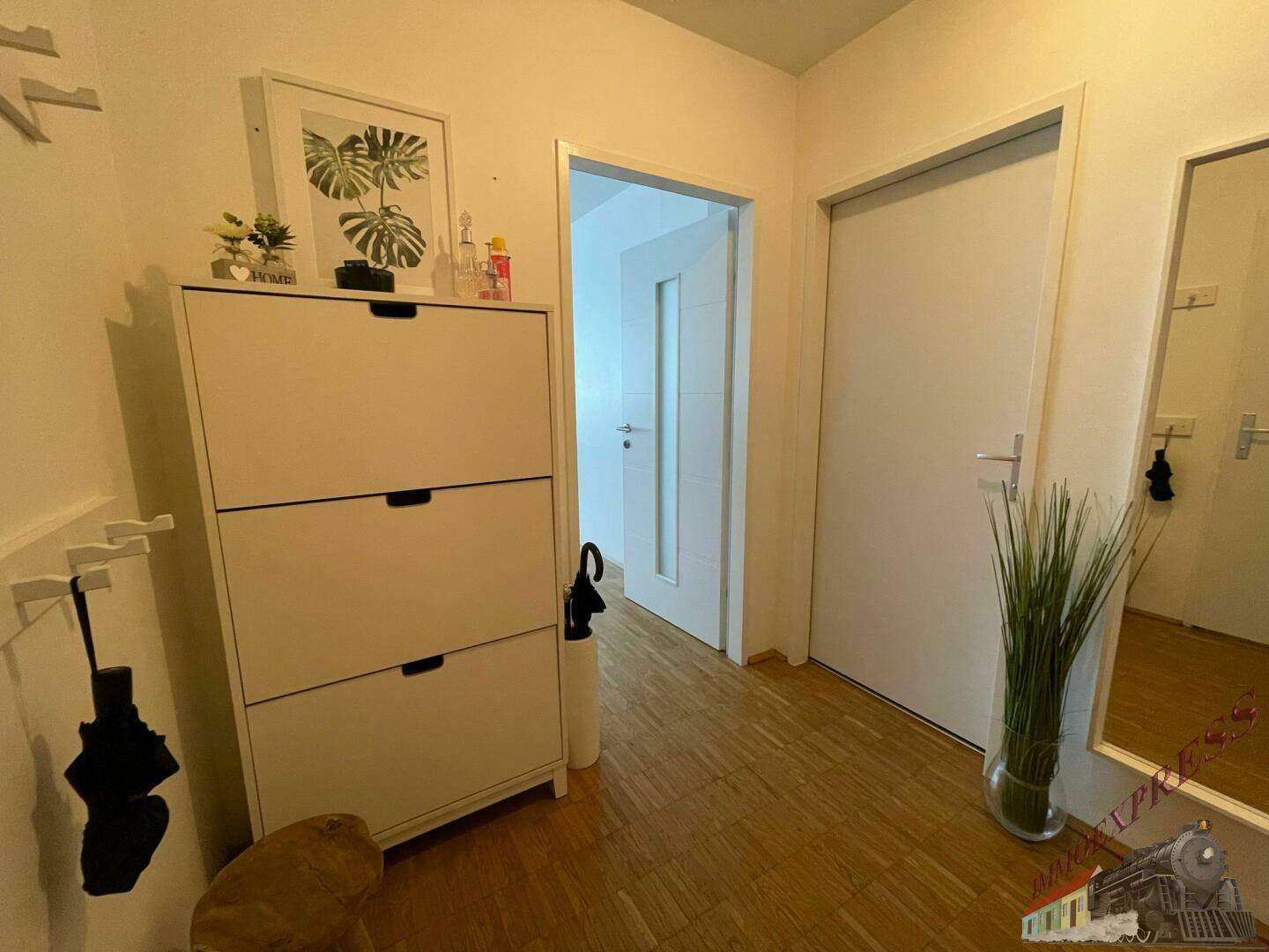 Heller Flur mit Schuhschrank, Spiegel und Holzboden, der zu weiteren Räumen führt.