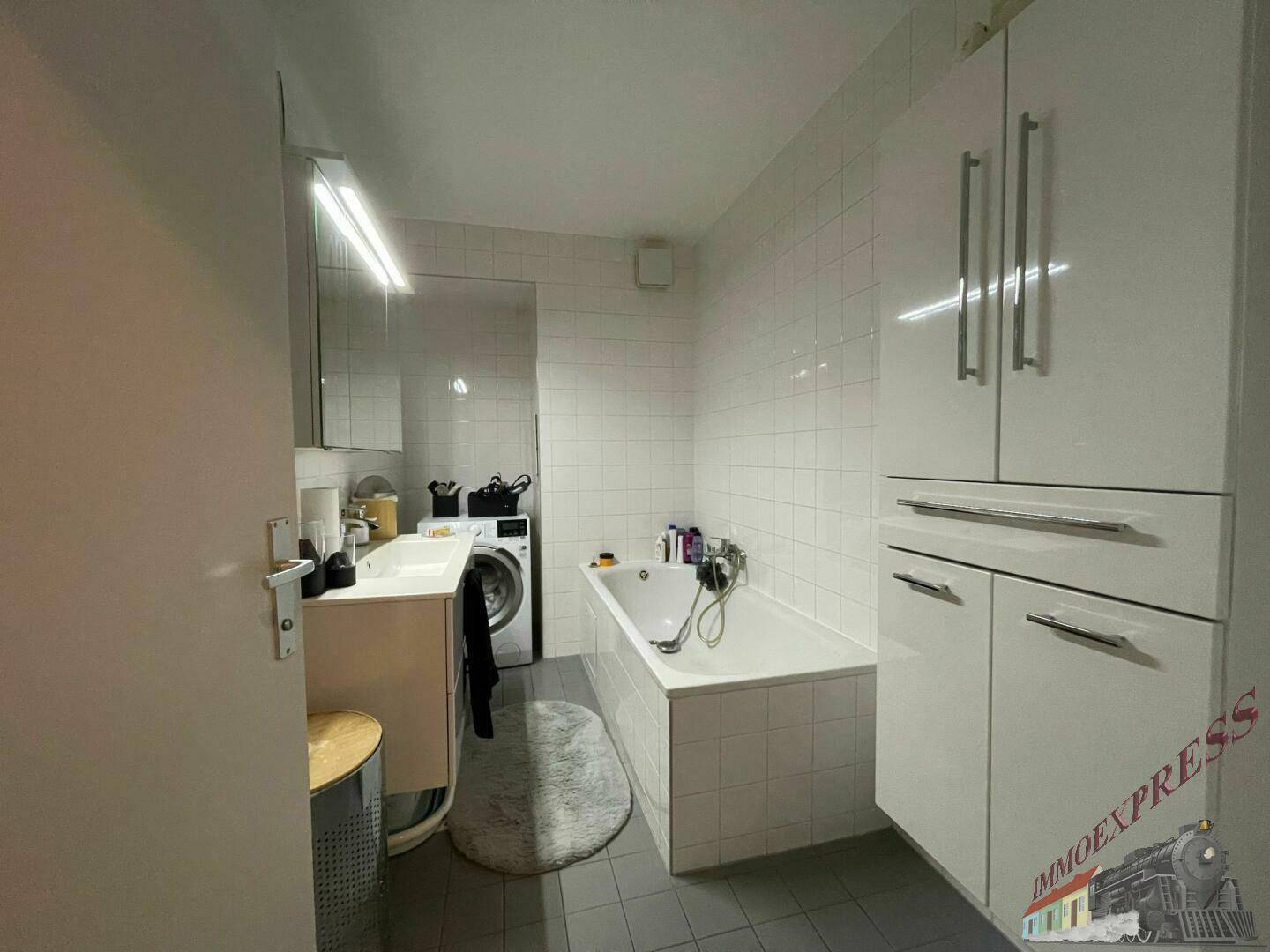 Modernes Badezimmer mit Badewanne, Waschbecken und Waschmaschine in hellen Fliesen.