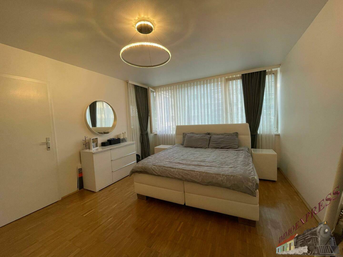 Helles Schlafzimmer mit modernem Doppelbett, Kommode und runden Deckenleuchten.