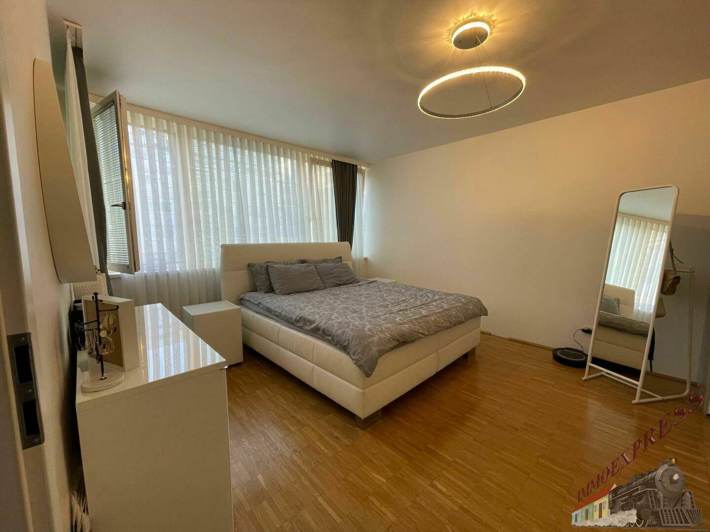 Schlafzimmer mit Doppelbett, Nachttischen und großen Fenstern mit Vorhängen für viel Licht.