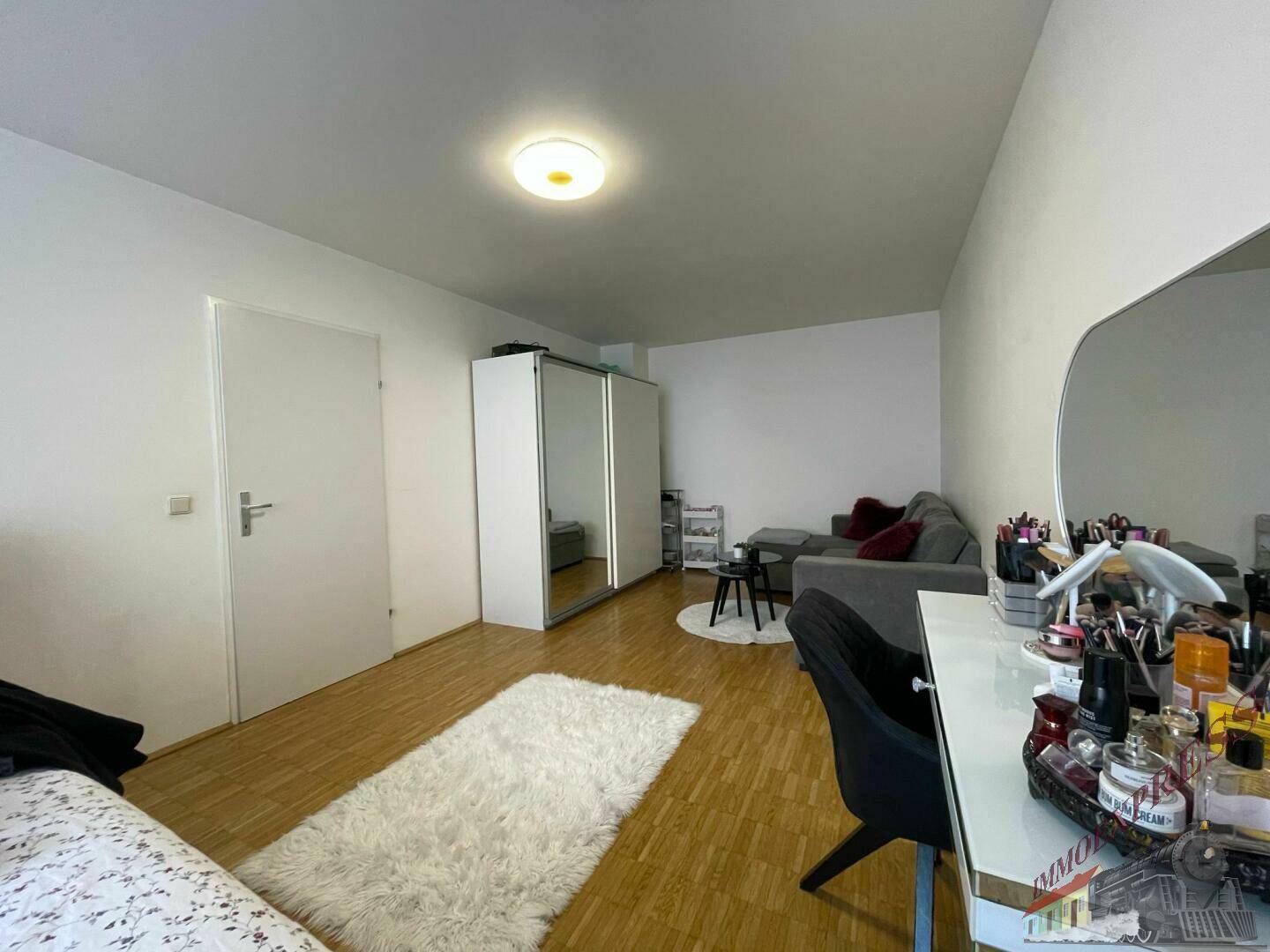 Heller Wohnraum mit Sofa, Spiegelschrank und weichem Teppich auf Holzboden.