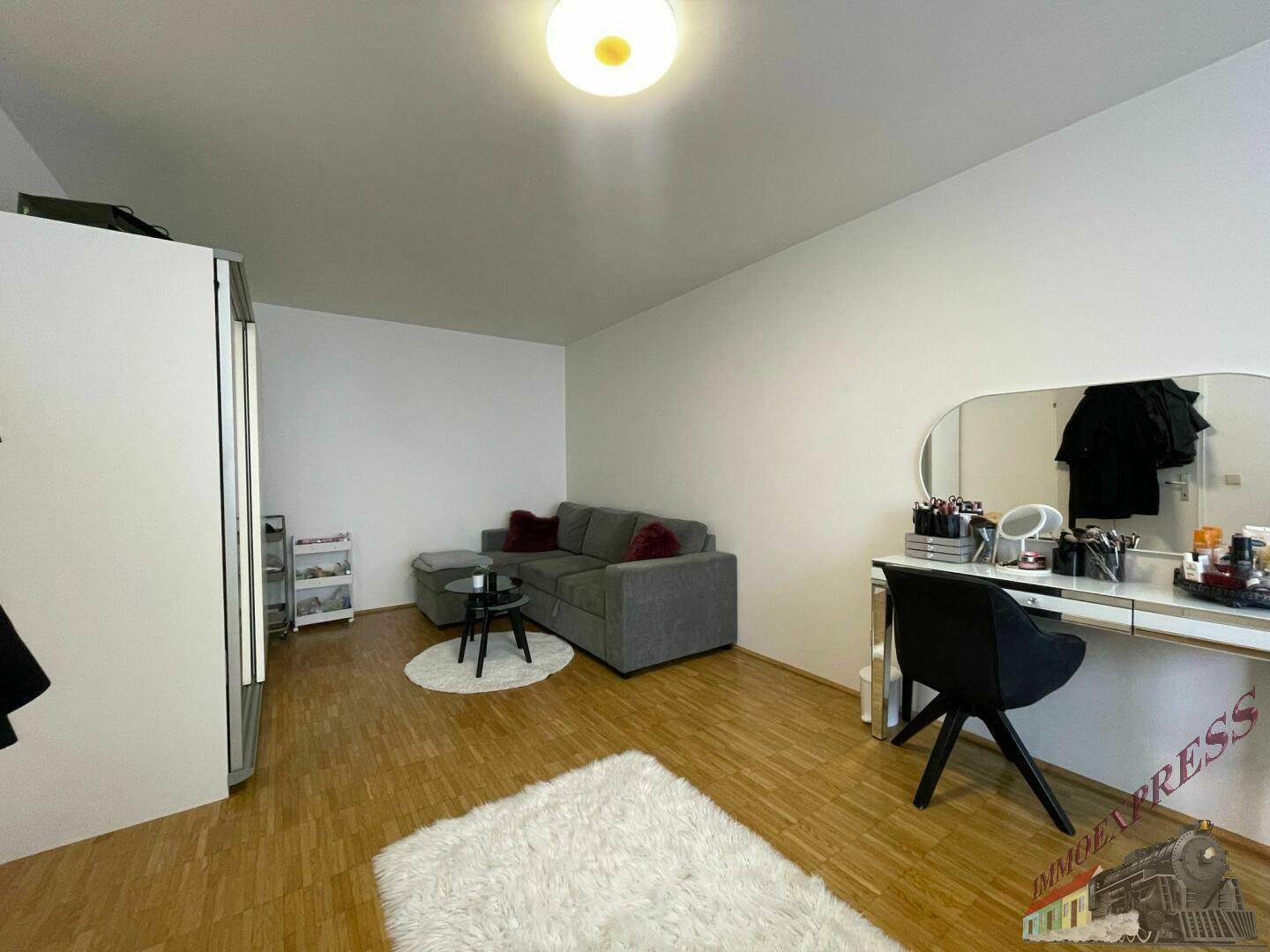 Gemütlicher Wohnbereich mit Sofa, Schminktisch und hellem Holzboden, gut beleuchtet.