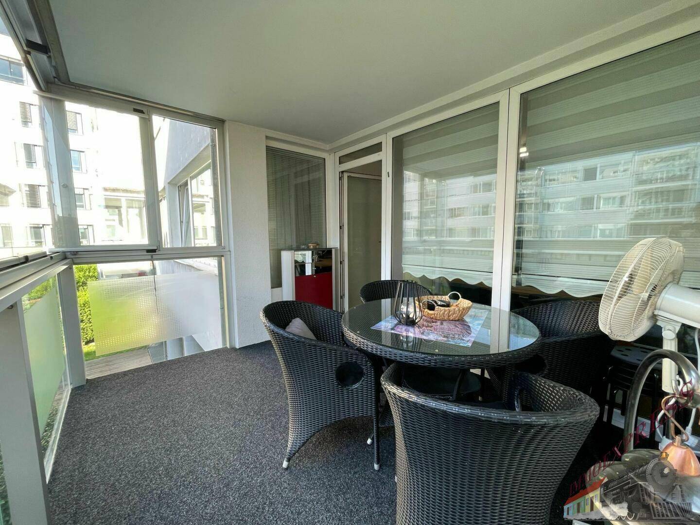 Verglaster Balkon mit gemütlicher Sitzecke und Blick auf die moderne Architektur der Umgebung.