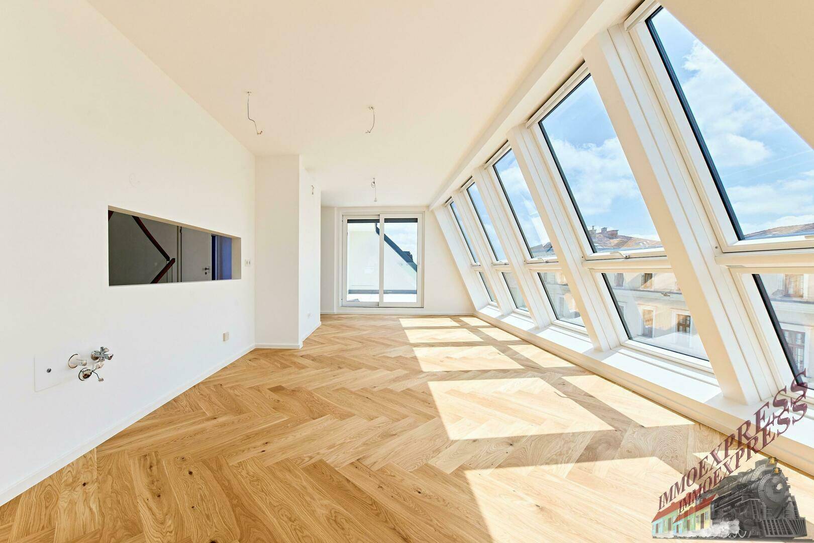 Heller Wohnraum mit Fischgrätparkett und großen schrägen Fenstern, die viel Tageslicht hereinlassen.