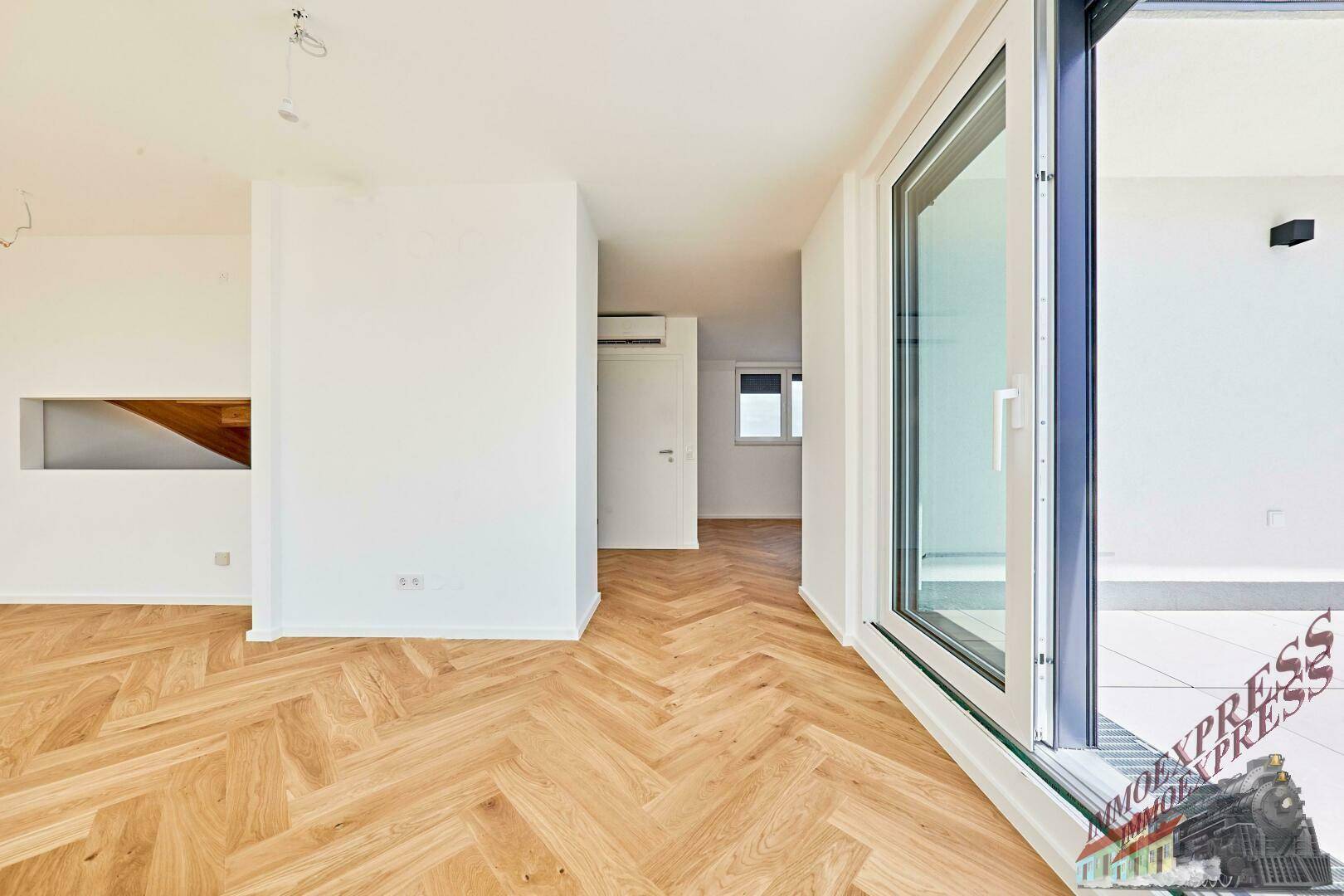 Heller Wohnraum mit Fischgrätparkett und Zugang zu einem Balkon, bietet viel Tageslicht.