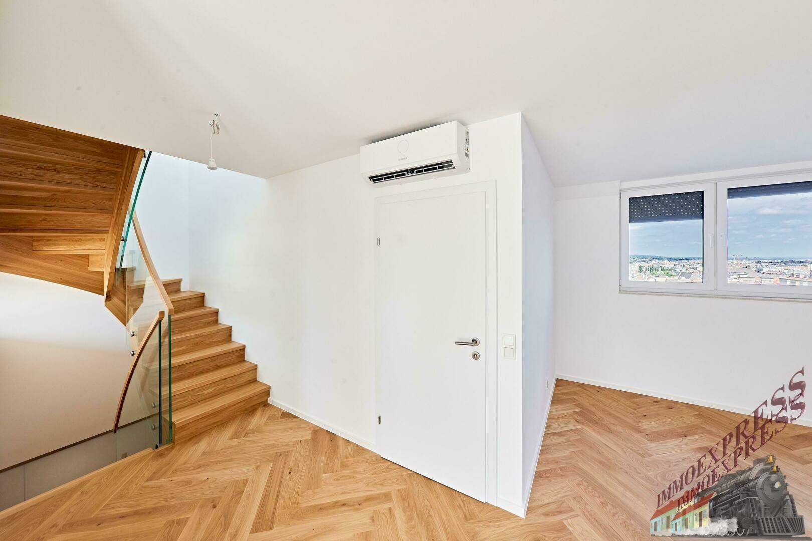 Heller Wohnraum mit Fischgrätparkett, Klimaanlage und Zugang zu einer Holztreppe.