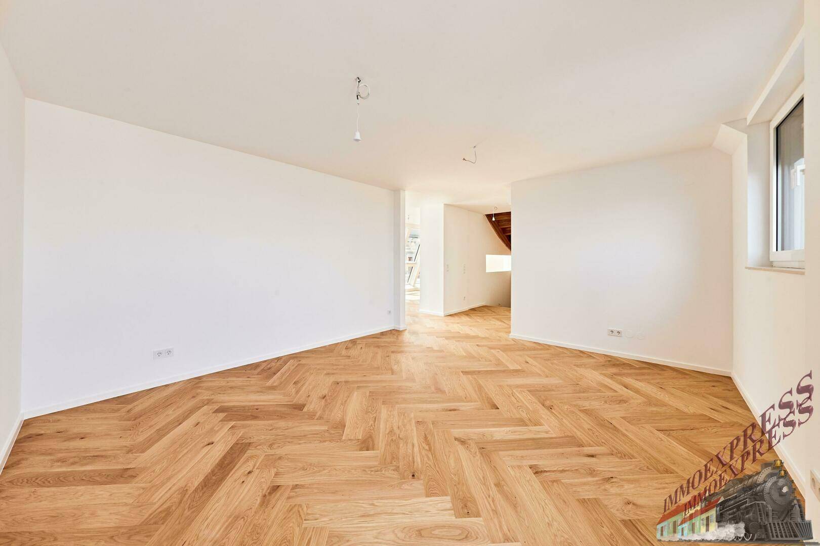 Geräumiger Wohnraum mit Fischgrätparkett und weißen Wänden, bereit zur individuellen Einrichtung.