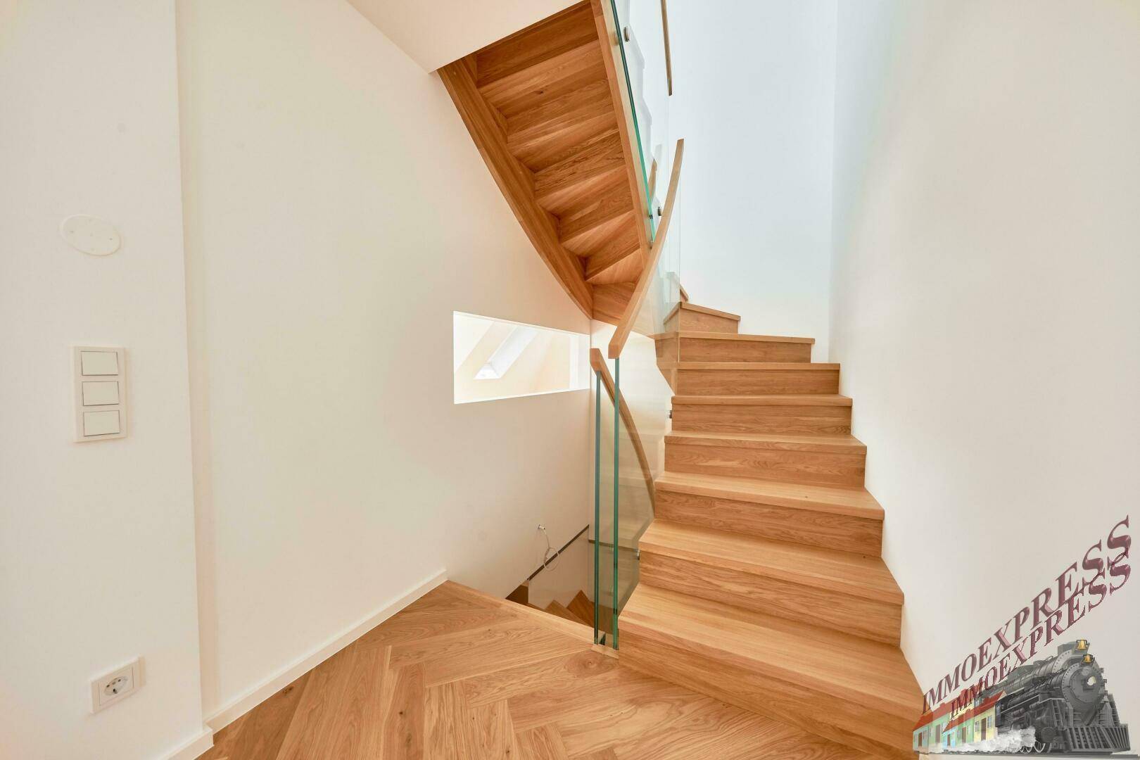 Elegante Holztreppe mit Glasgeländer, die zu den oberen Etagen der Wohnung führt.