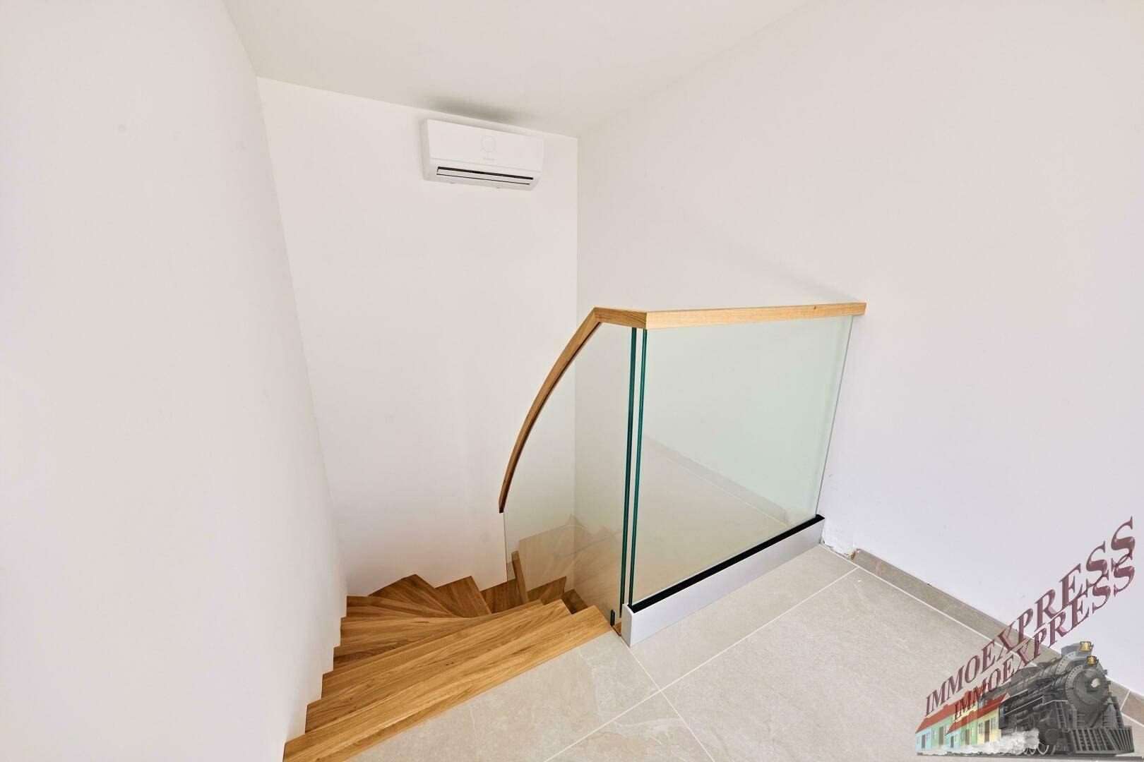 Moderne Holztreppe mit Glasgeländer und Klimaanlage in einem hellen Treppenhaus.