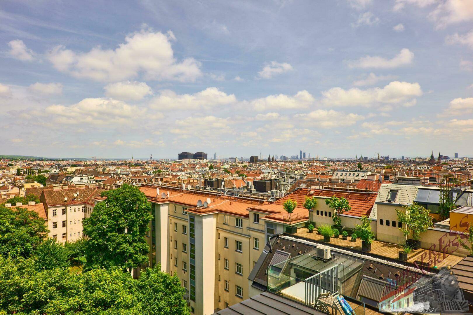 Panoramablick über die Stadt mit vielen Dächern, Bäumen und einem weiten Horizont.