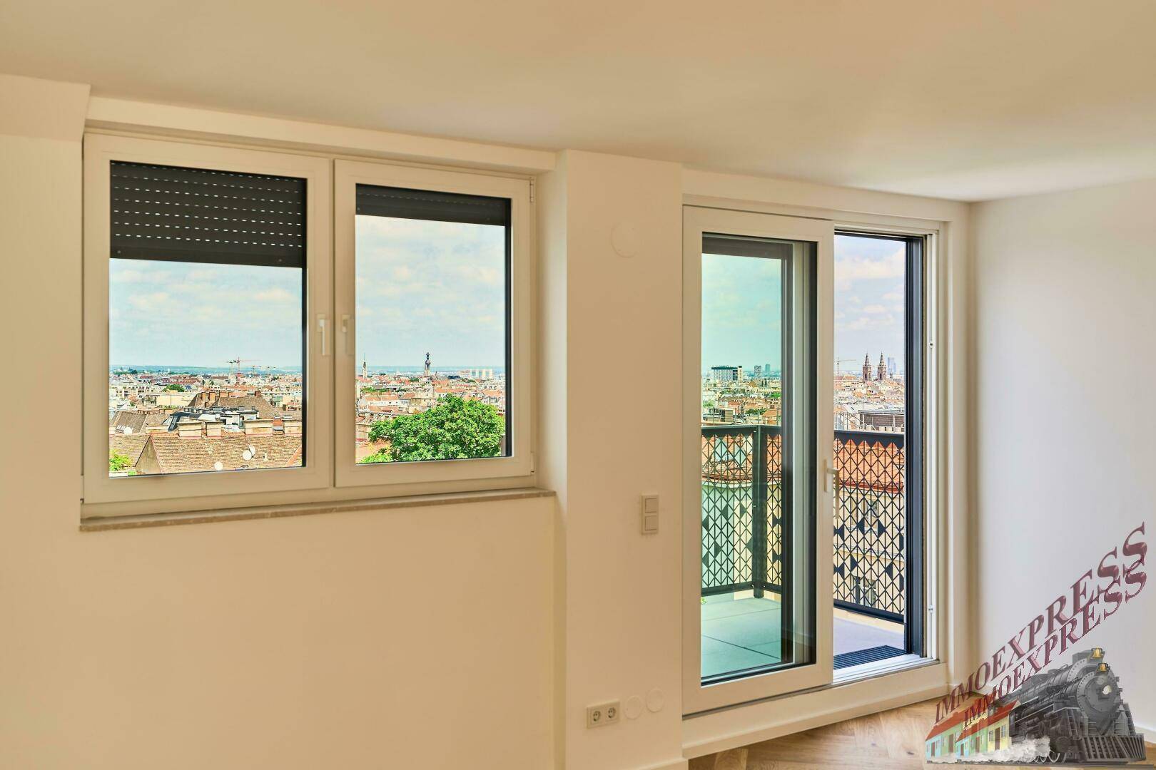 Heller Raum mit Parkettboden, großen Fenstern und Zugang zu einem Balkon mit Stadtblick.