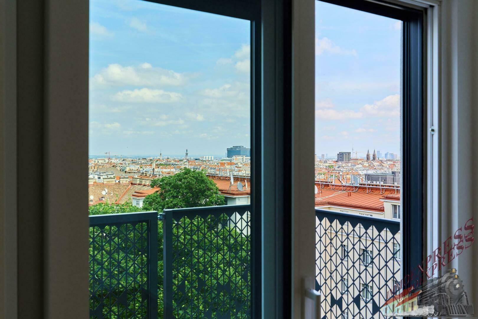 Blick aus dem Fenster auf die Stadtlandschaft mit roten Dächern und blauem Himmel.